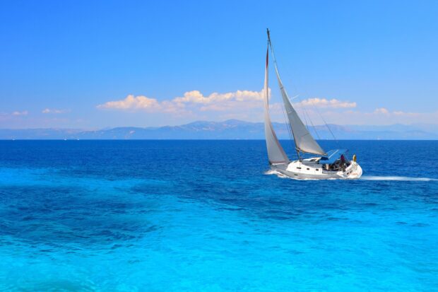 A sail boat gliding across the blue sea under a clear sky with distant mountains
