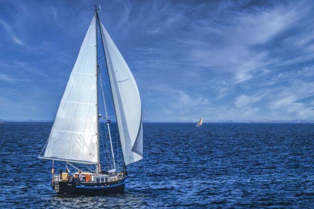 A sail boat with white sails sailing on the deep blue sea under a clear sky