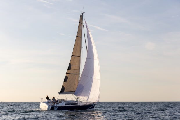 A sail boat gliding on the sea with white and brown sails during sunset