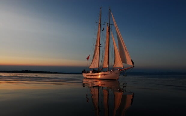 A sail boat sailing calmly during sunset with clear reflections on the water