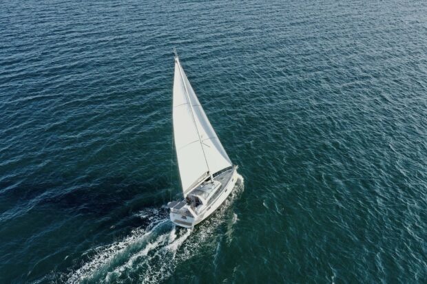 A sail boat sailing on the open ocean with clear blue water surrounding it
