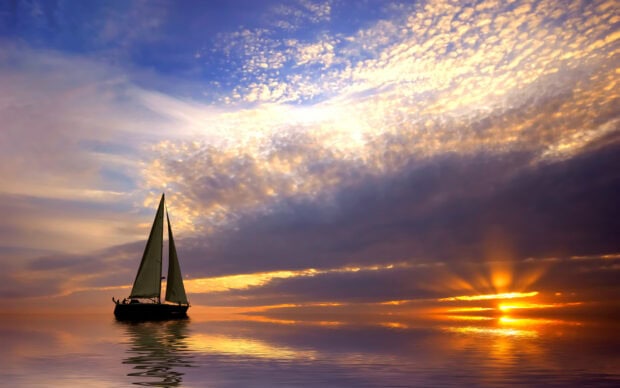 A sail boat sailing peacefully on calm water during a colorful sunset sky