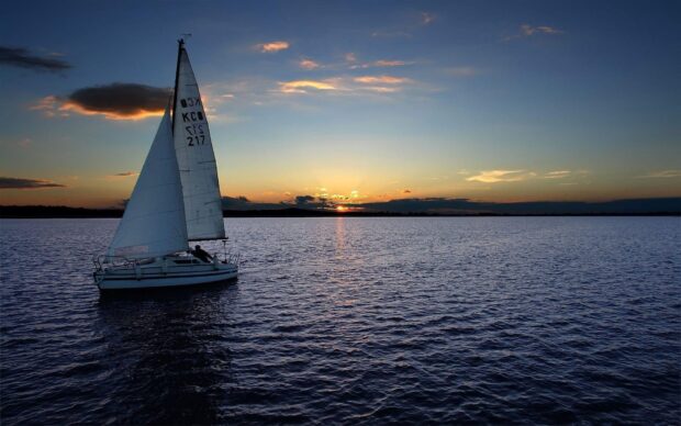 A sail boat sailing on calm water during sunset with a clear sky