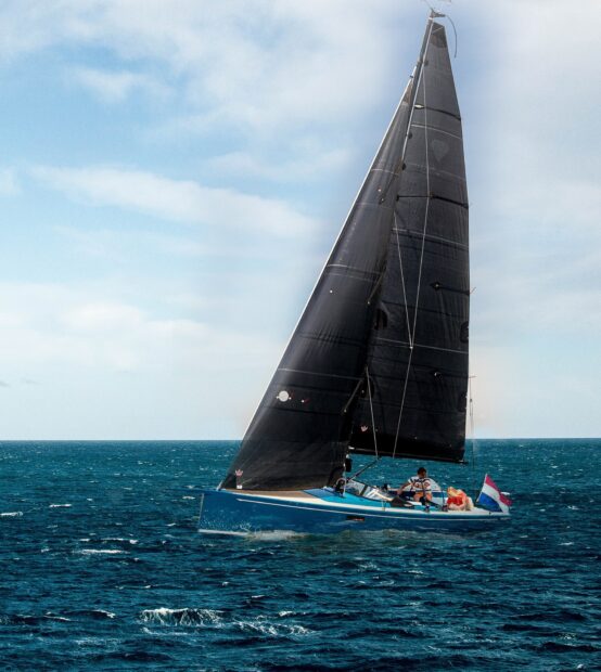 Black sail boat sailing on the ocean with people on board and a clear sky