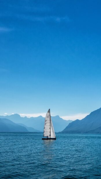 A sail boat gliding on the calm blue water with mountains in the background