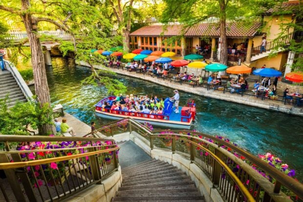 A riverwalk scene in San Antonio Texas with a tour boat and colorful umbrellas along the waterway