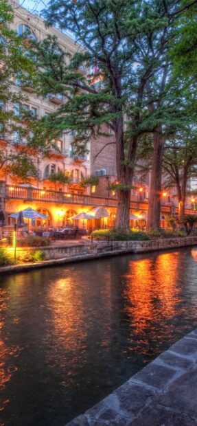 Evening view of San Antonio Texas riverwalk with trees and illuminated restaurants