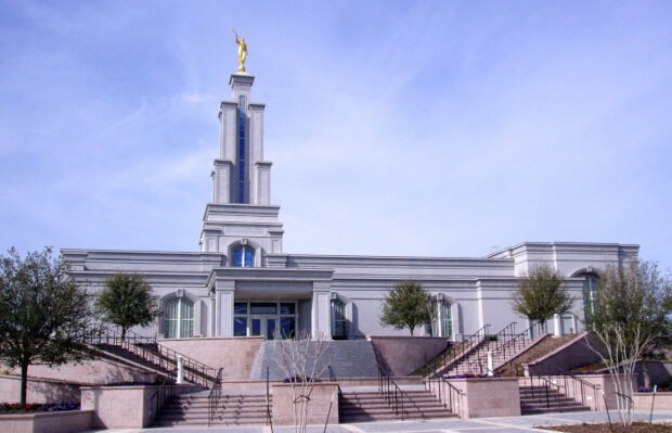 The San Antonio Texas temple stands tall under a clear blue sky with surrounding trees and stairs