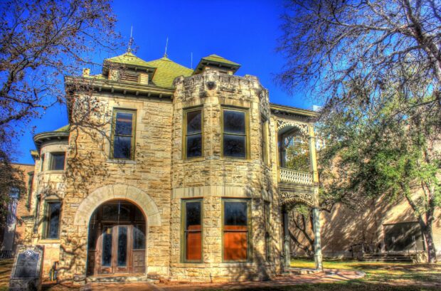 Historic San Antonio Texas building made of stone with large windows and a green roof surrounded by trees