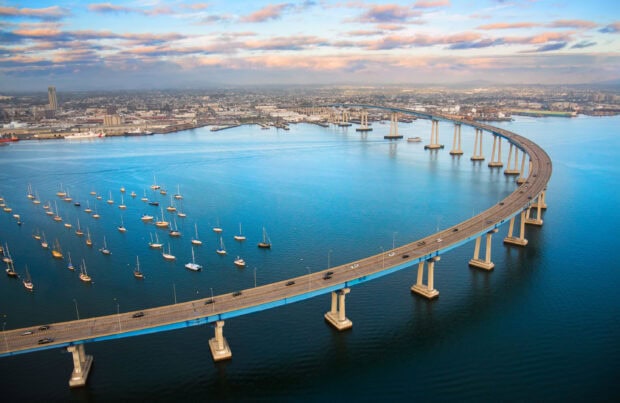 Aerial view of San Diego cityscape with a curved bridge over blue water and anchored boats