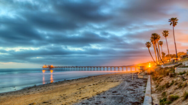 A scenic view of a San Diego pier at sunset with palm trees and cloudy sky