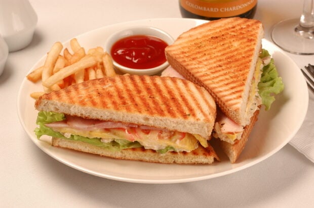 Grilled sandwich with ham lettuce and tomato served with fries and ketchup on a plate