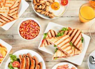 Grilled sandwich with lettuce and tomato served with breakfast sides on wooden table