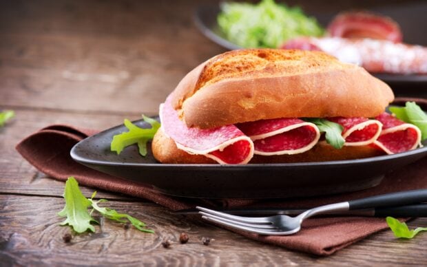 A sandwich with slices of salami and fresh greens on a rustic plate