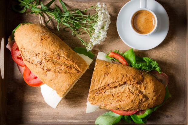 Fresh sandwich with tomato lettuce and cheese on a wooden tray with coffee and flowers