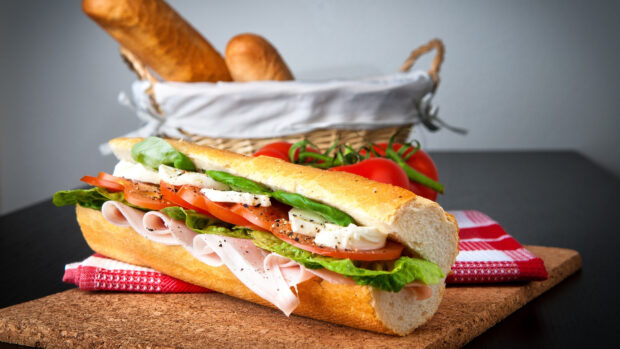 Fresh sandwich with lettuce tomato and deli meat on a baguette with tomatoes in the background