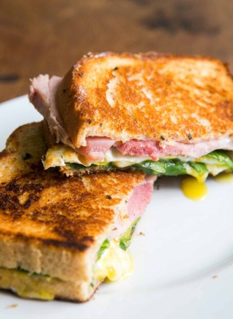 A grilled sandwich with ham spinach and melted cheese on a white plate