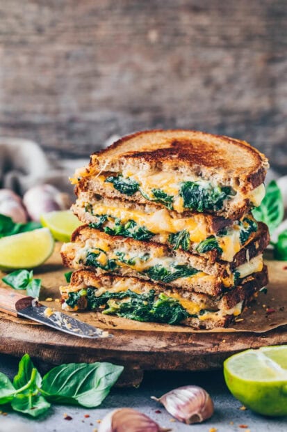 Toasted sandwich with melted cheese and fresh spinach stacked on wooden board