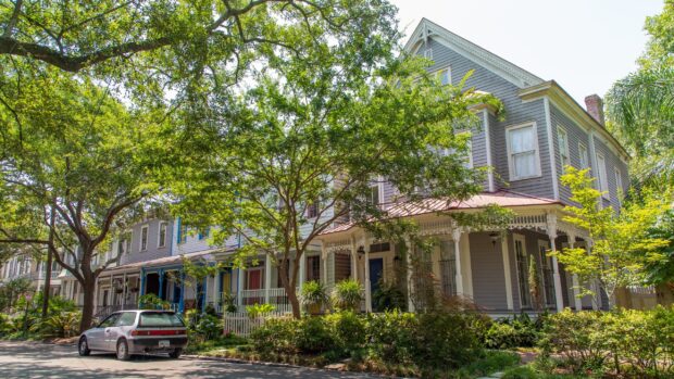 A quiet street in Savannah Georgia with historic houses and lush green trees lining the sidewalk