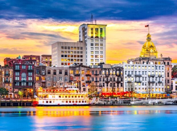 Historic Savannah Georgia cityscape with riverboat and colorful sunset sky