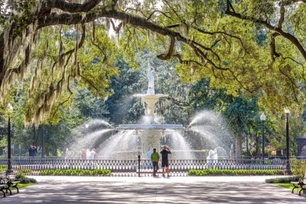 The fountain in Savannah Georgia park surrounded by moss covered trees and visitors