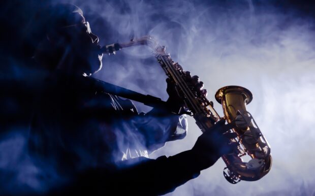 A musician playing a saxophone surrounded by smoke in a dark setting