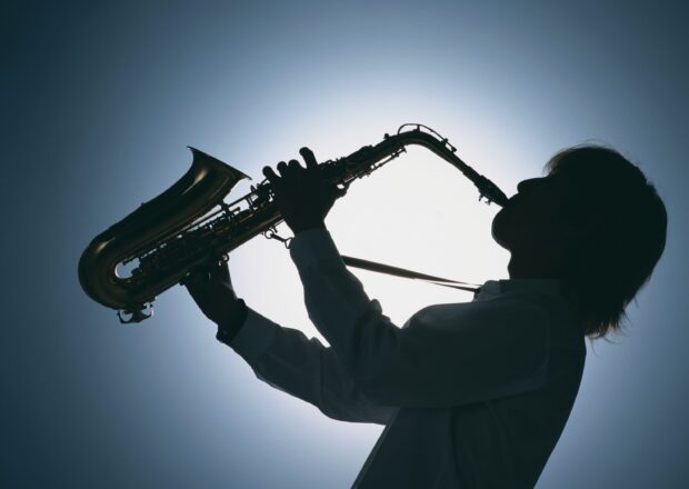 A silhouette of a person playing saxophone against a bright sky background