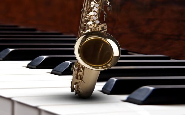 A brass saxophone resting on black and white piano keys in a close up view