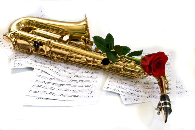 Golden saxophone with a red rose lying on music sheets on a white surface