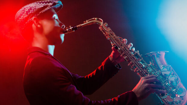 Young musician playing saxophone under colorful stage lighting