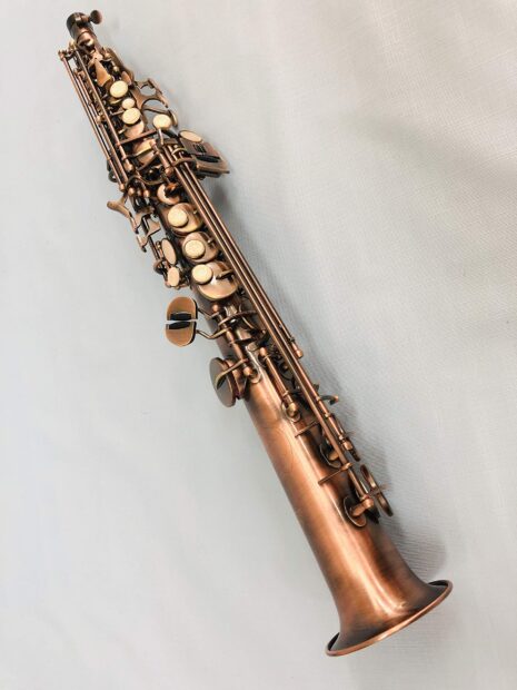 A bronze saxophone lying on a light textured surface with clear detailed keys and valves