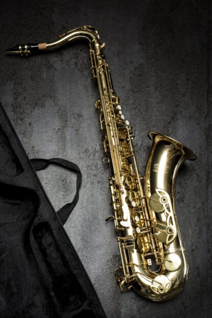 A gold saxophone resting next to an open black case on a textured surface