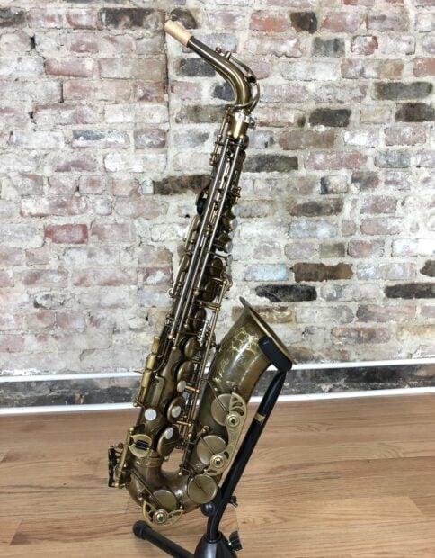 A vintage saxophone resting on a stand against a brick wall background