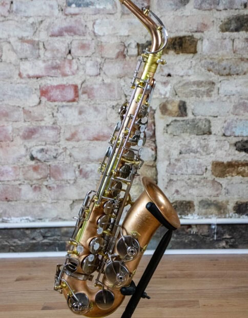 A vintage saxophone resting on a stand against a rustic brick wall background