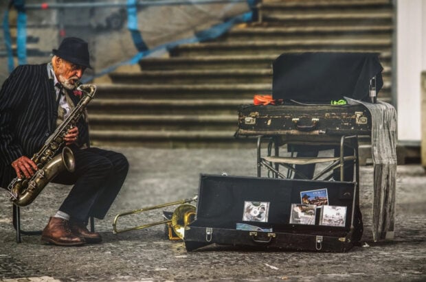 An elderly man playing saxophone on the street with his musical instruments in an urban setting