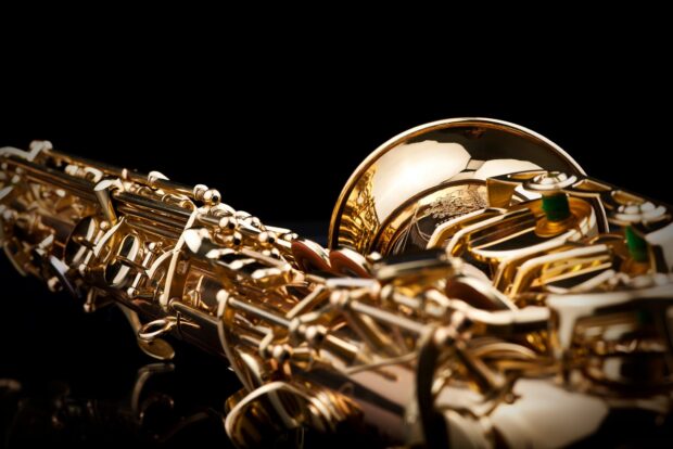 Close up of a saxophone showing detailed keys and shiny brass surface against black background