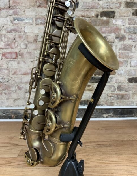 Vintage brass saxophone resting on a wooden floor with a rustic brick wall background