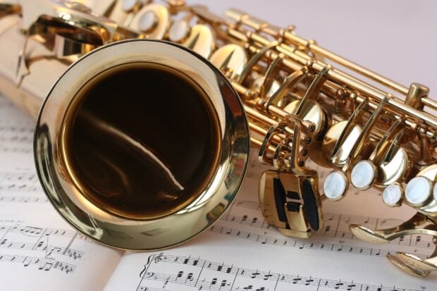 Close up view of a saxophone lying on sheet music with detailed keys and bell
