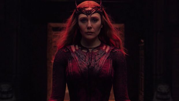 Scarlet Witch character stands with a focused expression in a dark setting wearing a detailed costume