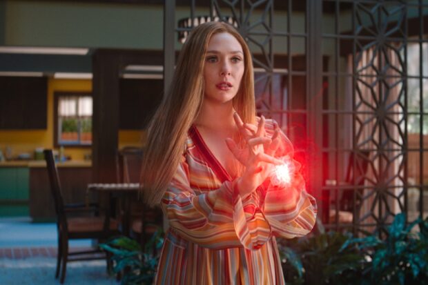 Scarlet Witch using her magic powers with a glowing red energy in a striped dress indoors