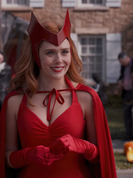 Scarlet Witch wearing a red costume and gloves smiling outdoors with red hair