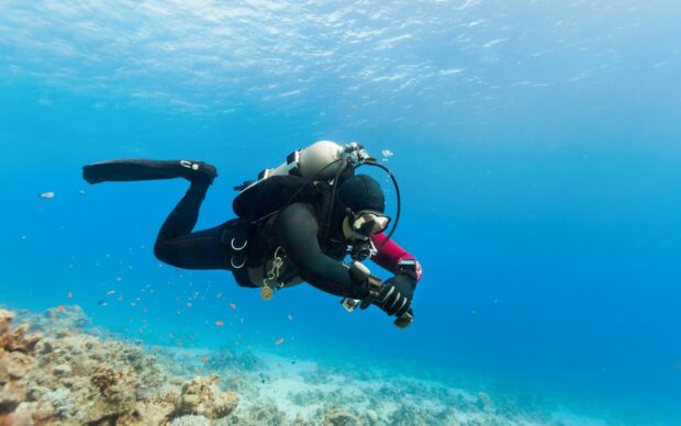 A scuba diver exploring coral reefs in clear blue water with advanced diving equipment