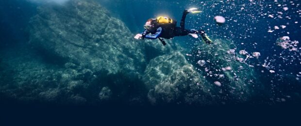 Scuba diver exploring underwater rocks and marine life in clear blue water