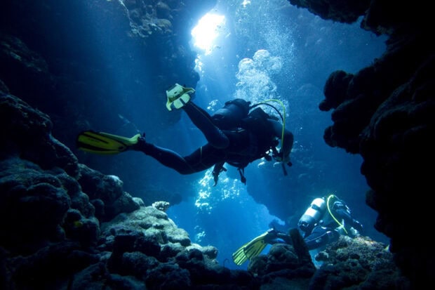 Scuba diving in a deep underwater cave surrounded by coral formations