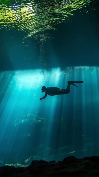 A scuba diver exploring underwater with light rays penetrating through the water surface