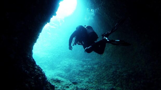 Scuba diving exploring underwater cave in deep ocean