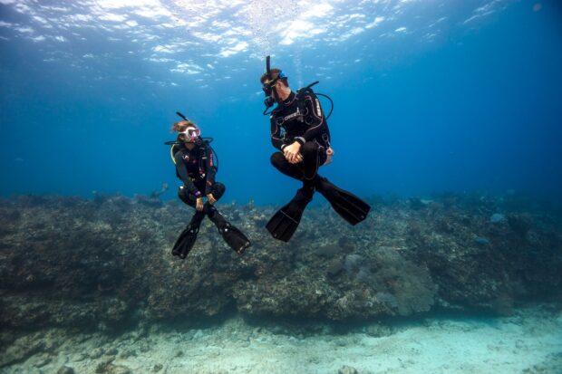 Two scuba divers exploring coral reef underwater in clear blue sea