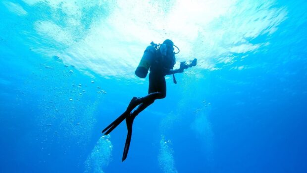 A scuba diver exploring deep blue ocean water with scuba gear and fins