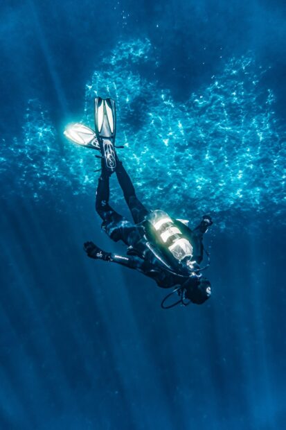 A scuba diver exploring underwater with fins and gear in clear blue water