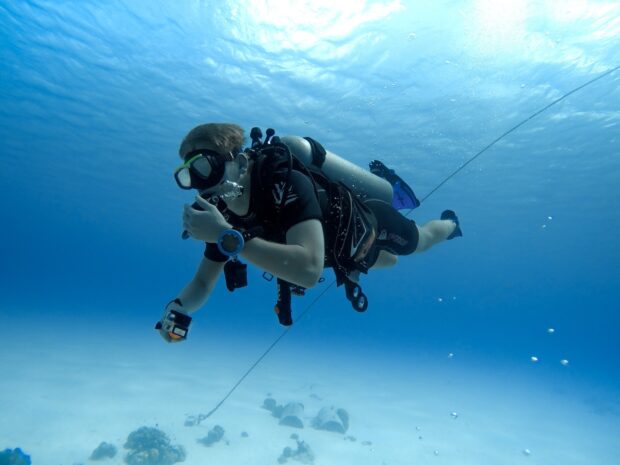 A scuba diver exploring underwater with scuba gear and watch in clear blue ocean